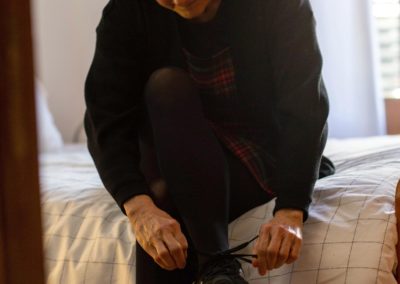 Vista general d'una dona cordant-se les sabates asseguda al llit