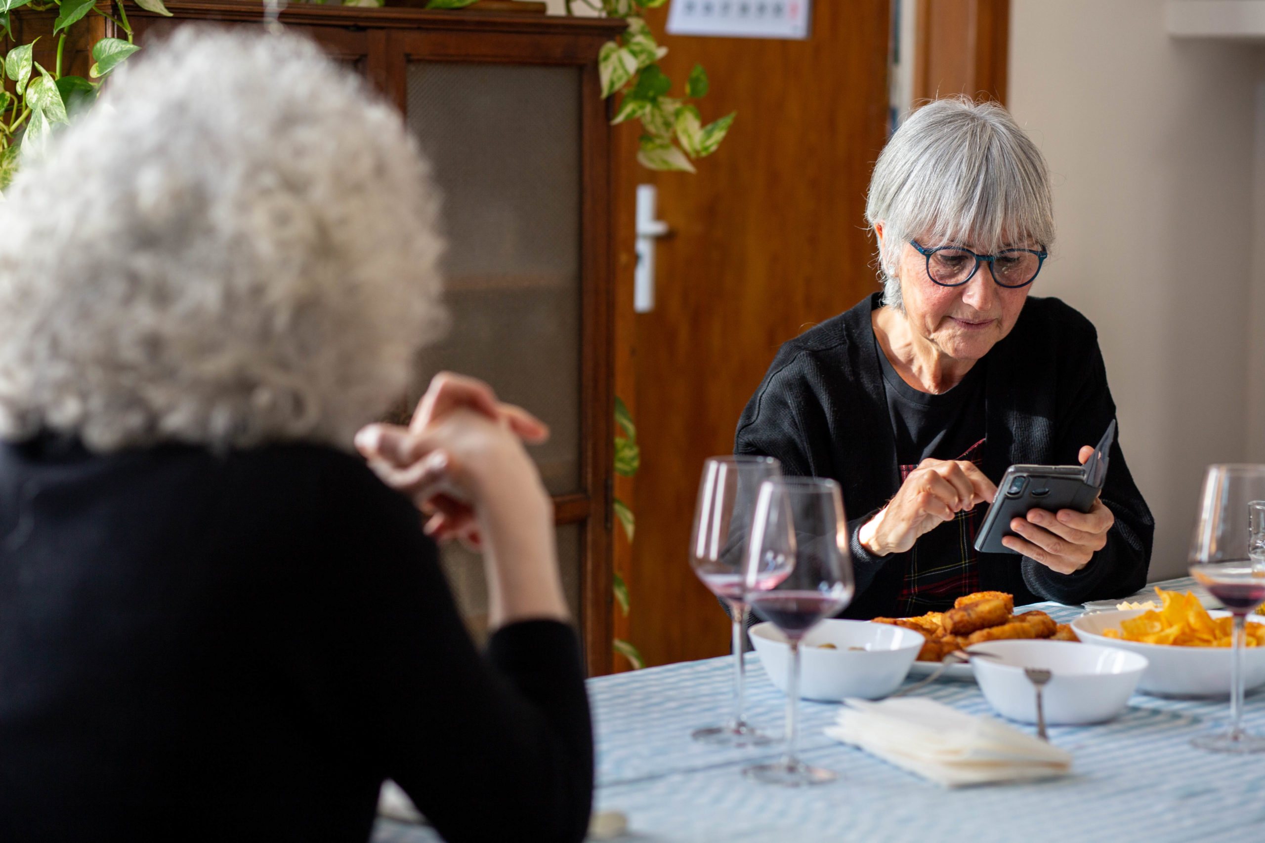 Pla mig d'una dona mirant el mòbil asseguda a la taula del menjador en un dinar