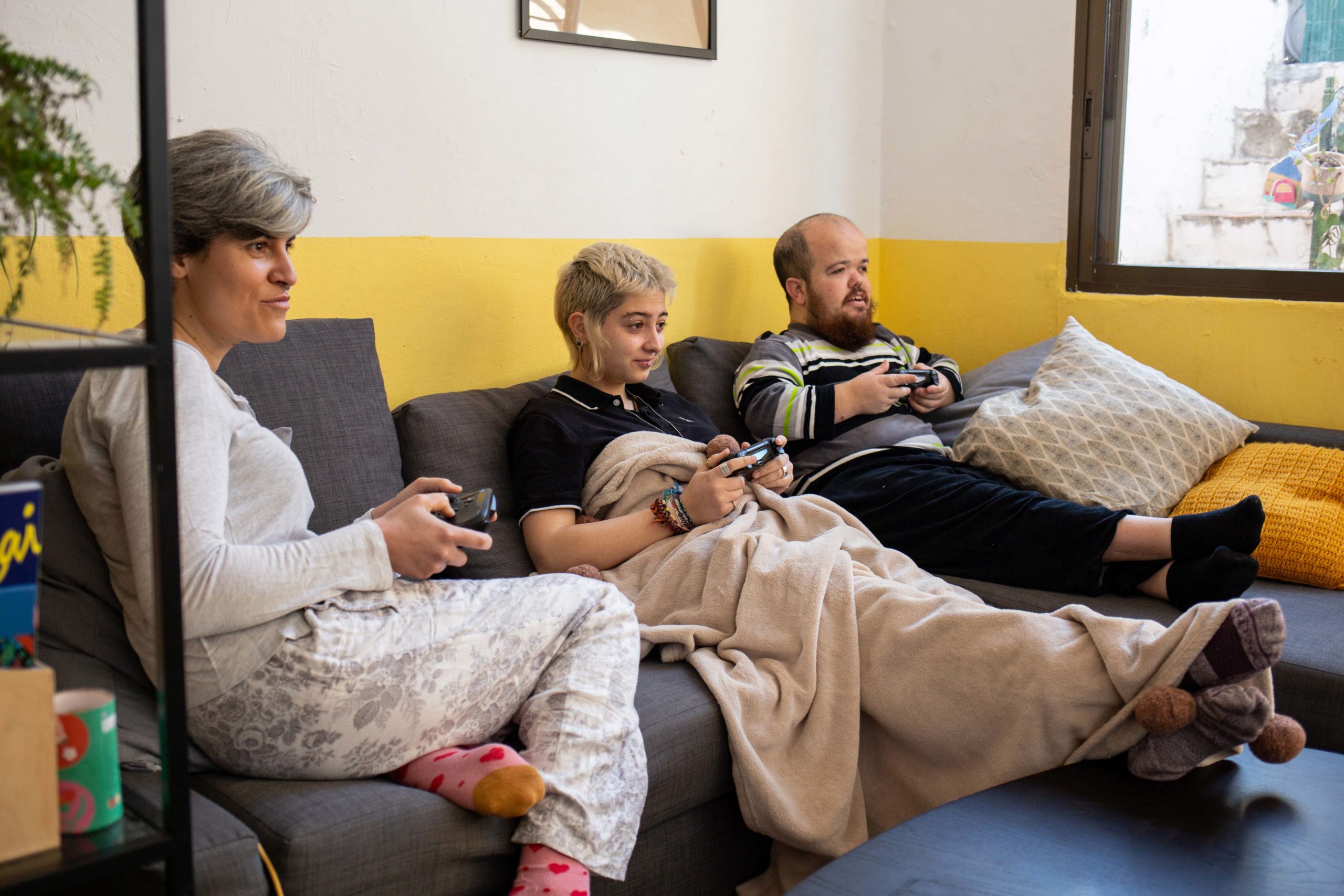 Tres companyes de pis jugant a un videojoc davant de la televisió i assegudes al sofà del menjador