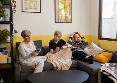 Tres companyes de pis jugant a un videojoc davant de la televisió i assegudes al sofà del menjador