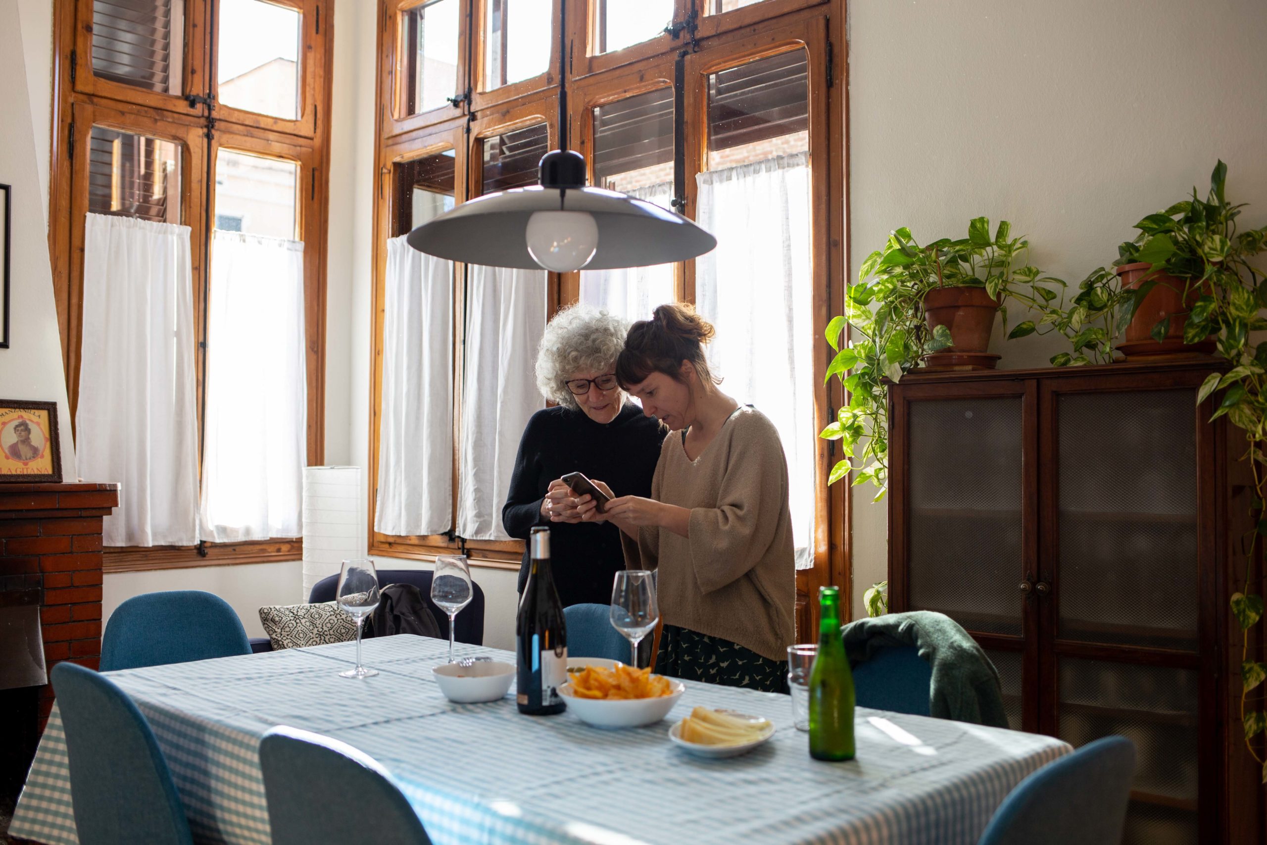 Vista general de dues dones mirant el mòbil al menjador de casa