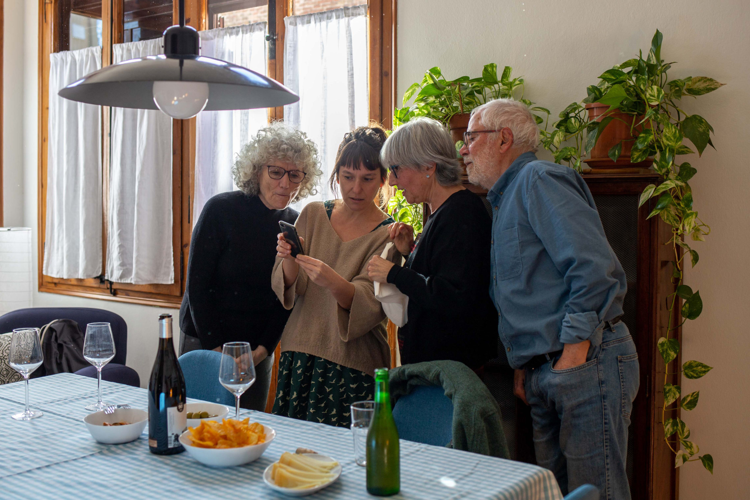 Vista general d'un grup d'amigues mirant el mòbil juntes al menjador de casa