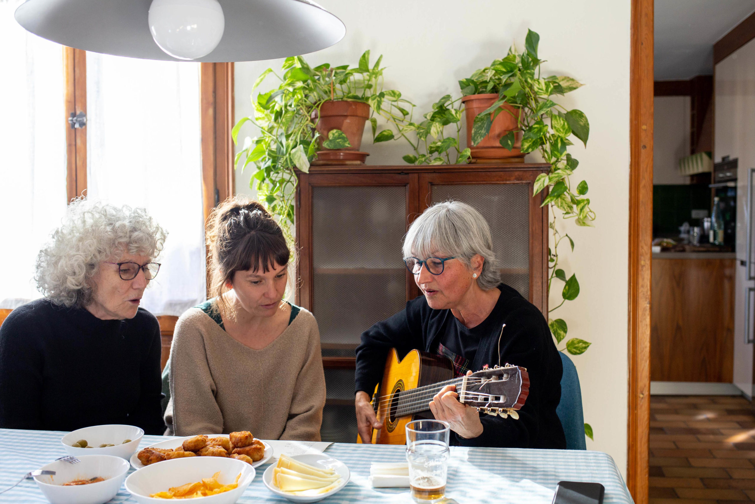 Tres amigues tocant la guitarra al menjador de casa