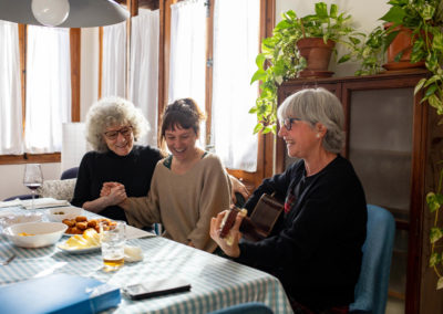 Tres amigues tocant la guitarra i rient al menjador de casa